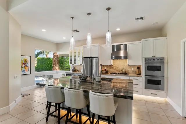 a kitchen with stainless steel appliances kitchen island granite countertop a table chairs and a refrigerator