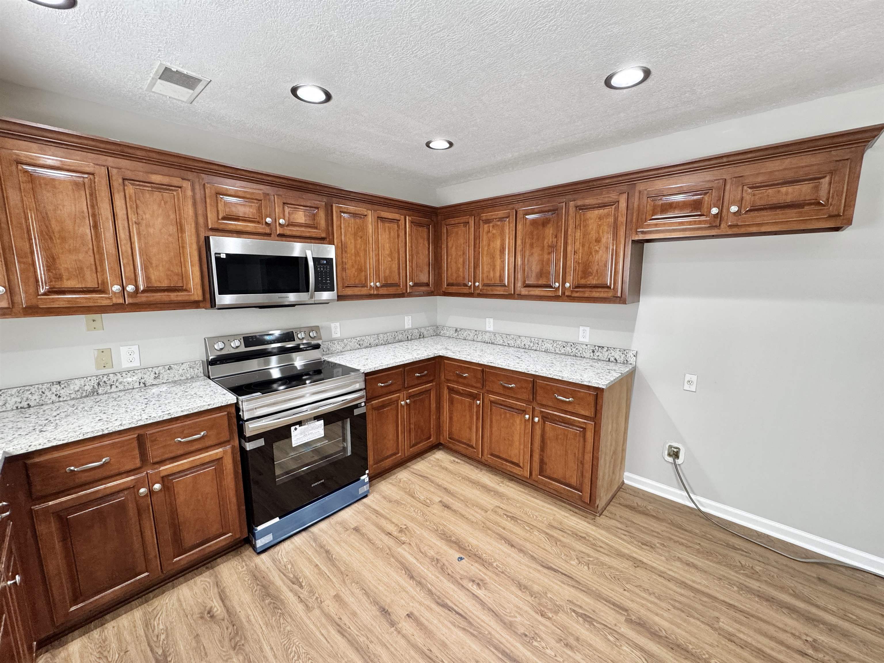 526 Stone Ridge Pinson, TN 38366 - Photo 6 of 39 Kitchen featuring stainless steel appliances, brown cabinets, light stone counters, a textured ceiling, and light wood-style floors