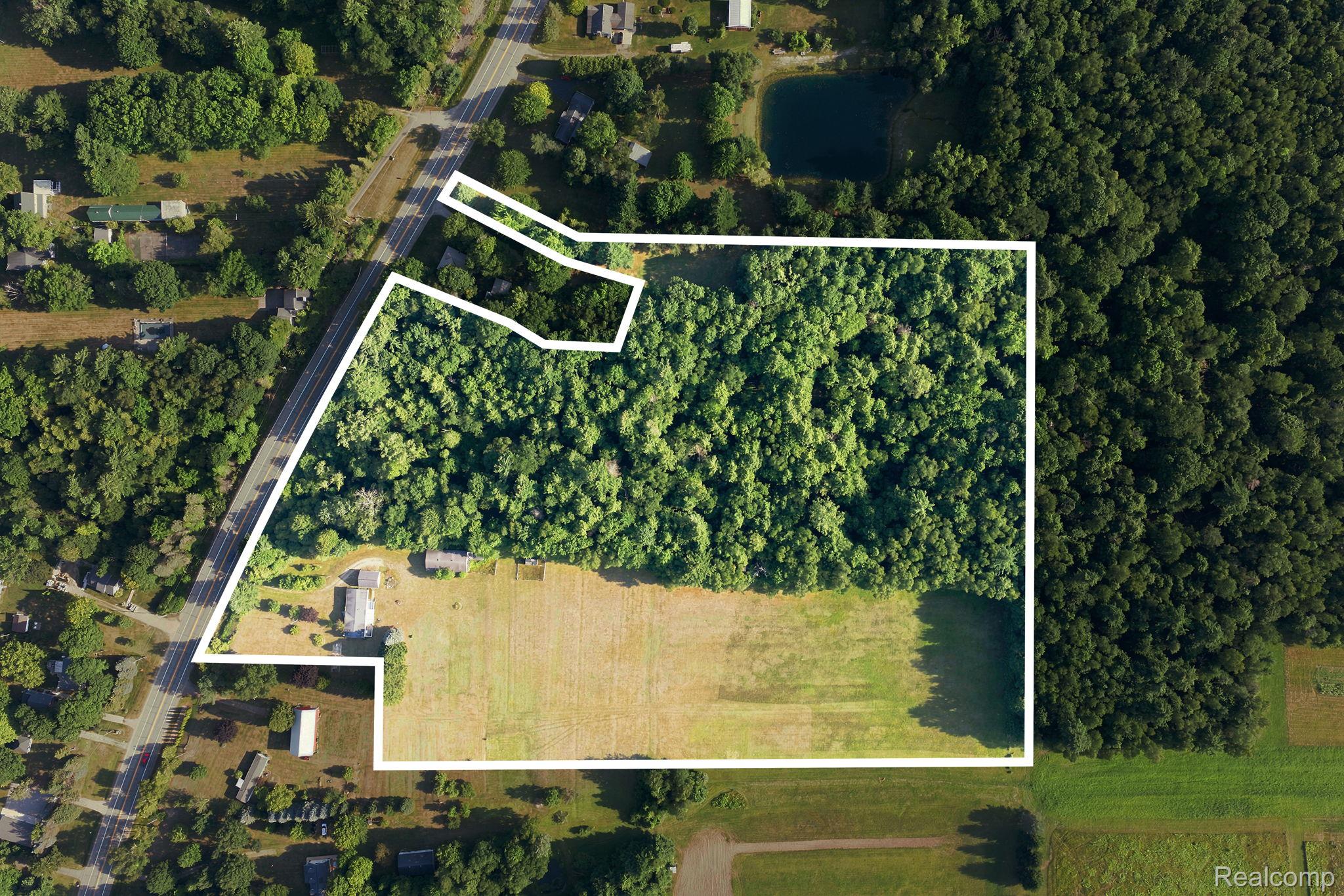 Expansive property featuring a mix of mature woodland and open fields, bordered by a paved roadway
