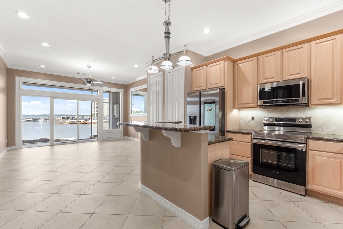 168 Lake Point Boulevard, Unit C102 Conroe, TX 77356 - Photo 3 of 35 Bright and spacious kitchen with modern stainless steel appliances, light wood cabinetry, and granite countertops. The open layout flows into a living area with large windows offering stunning waterfront views.