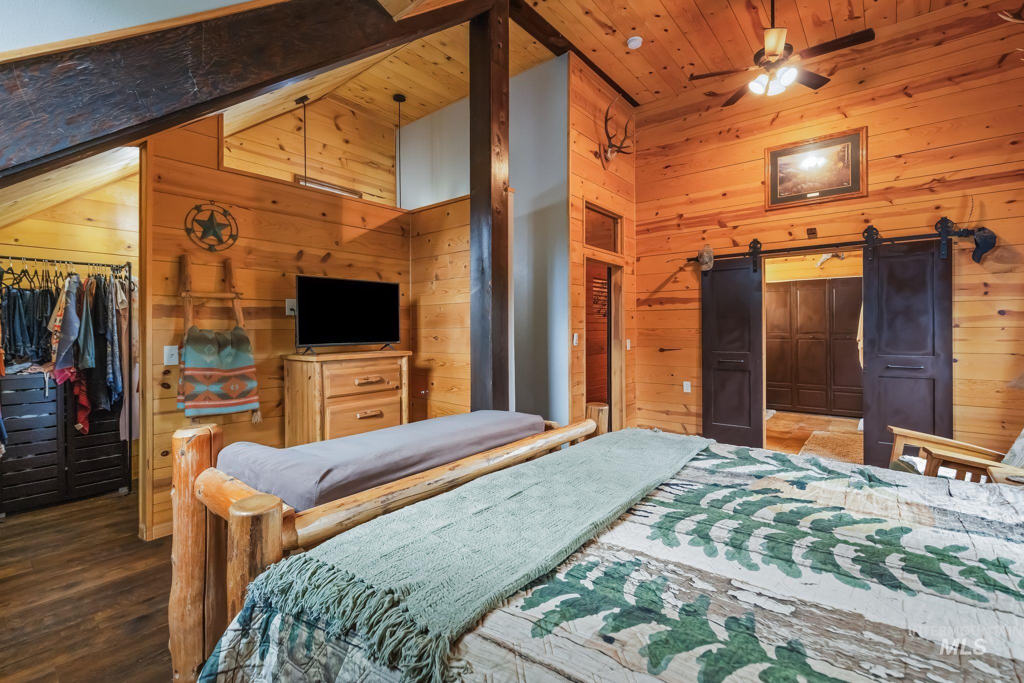 3989 East Mountain Road Anatone, WA 99401 - Photo 17 of 49 Wood-paneled walls and ceiling, exposed structural beam, ceiling fan, dark-finished barn doors, and built-in closet storage
