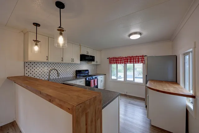 a kitchen with stainless steel appliances granite countertop a sink a microwave oven a refrigerator and white cabinets with wooden floor