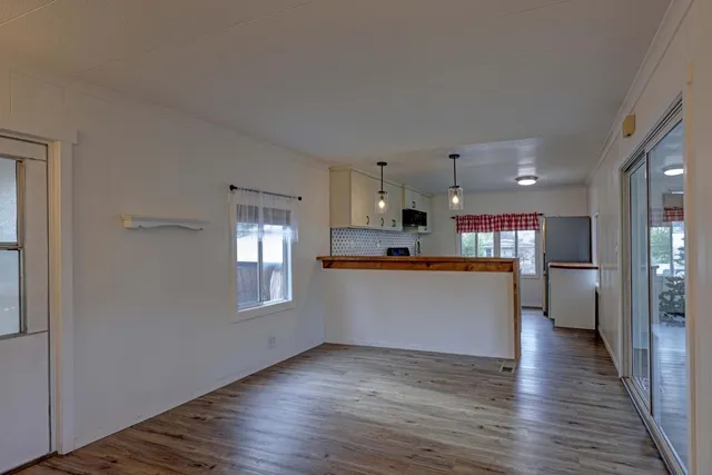 a view of an empty room and kitchen with wooden floor