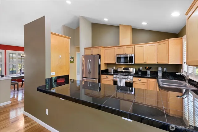 a kitchen with stainless steel appliances granite countertop a refrigerator a stove and a sink with wooden floor