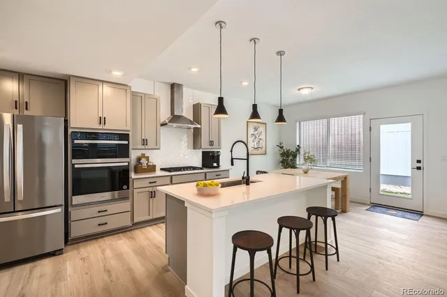 a kitchen with stainless steel appliances a stove a sink a microwave a refrigerator and white cabinets with wooden floor