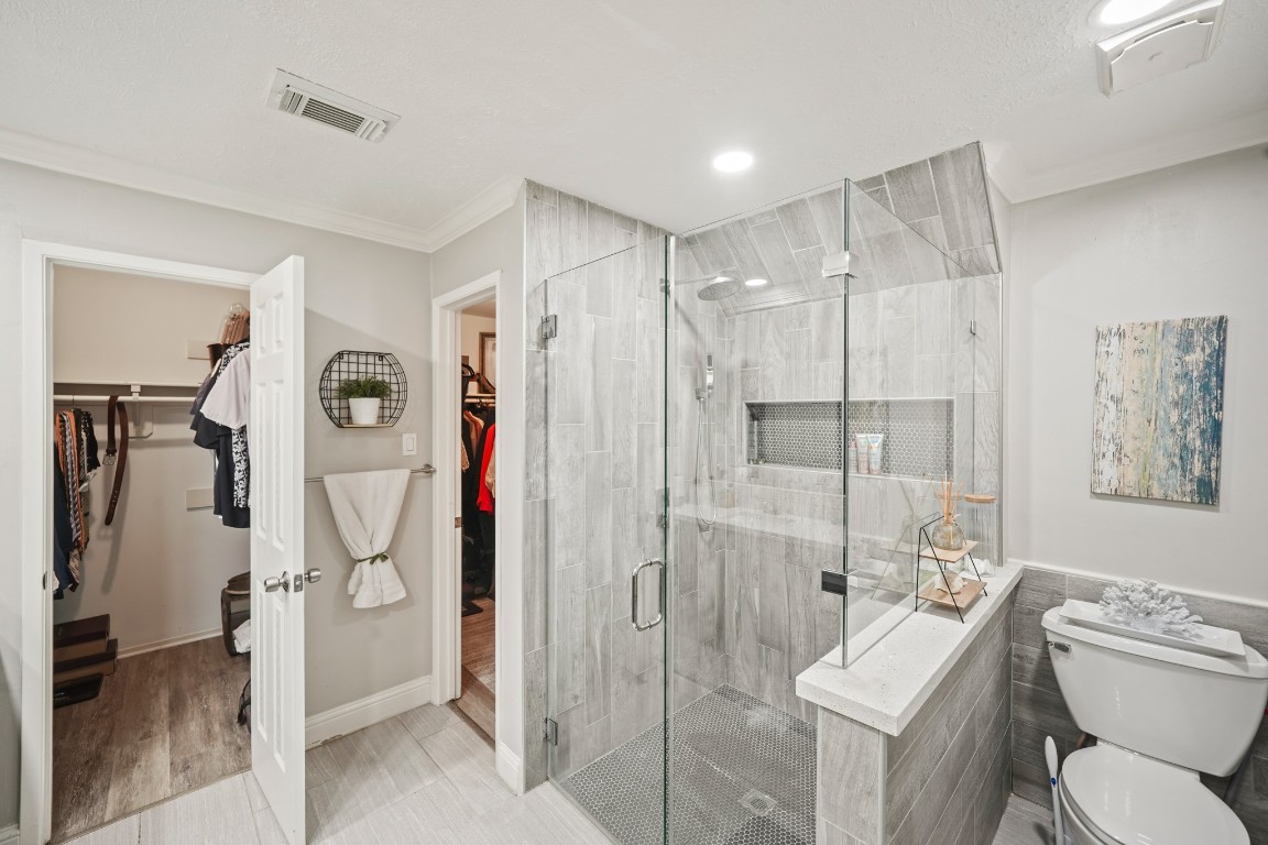 15831 Ridge Park Drive Houston, TX 77095 - Photo 10 of 26 Modern bathroom with a glass-enclosed shower, gray tile, and recessed lighting. It connects to a walk-in closet, offering a stylish and functional space.