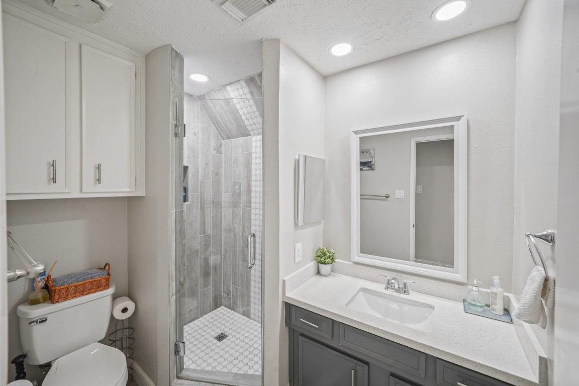 15831 Ridge Park Drive Houston, TX 77095 - Photo 16 of 26 This bathroom features a modern design with a glass-enclosed shower, sleek gray tiles, and a vanity with a white countertop. It includes ample storage with cabinets above the toilet and a large mirror above the sink, creating a bright and functional space.