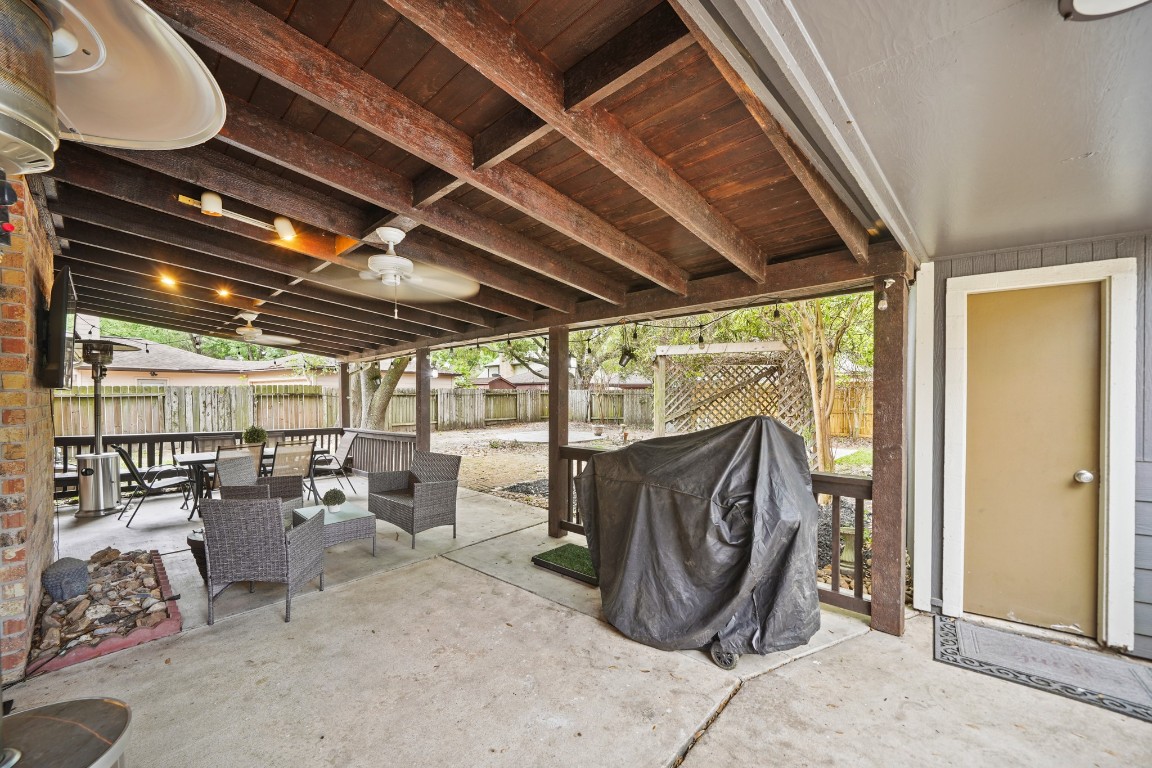 15831 Ridge Park Drive Houston, TX 77095 - Photo 18 of 26 This photo showcases a spacious, covered patio with wooden beams, outdoor seating, ceiling fans, and a barbecue grill, overlooking a fenced yard. Ideal for entertaining and relaxation.