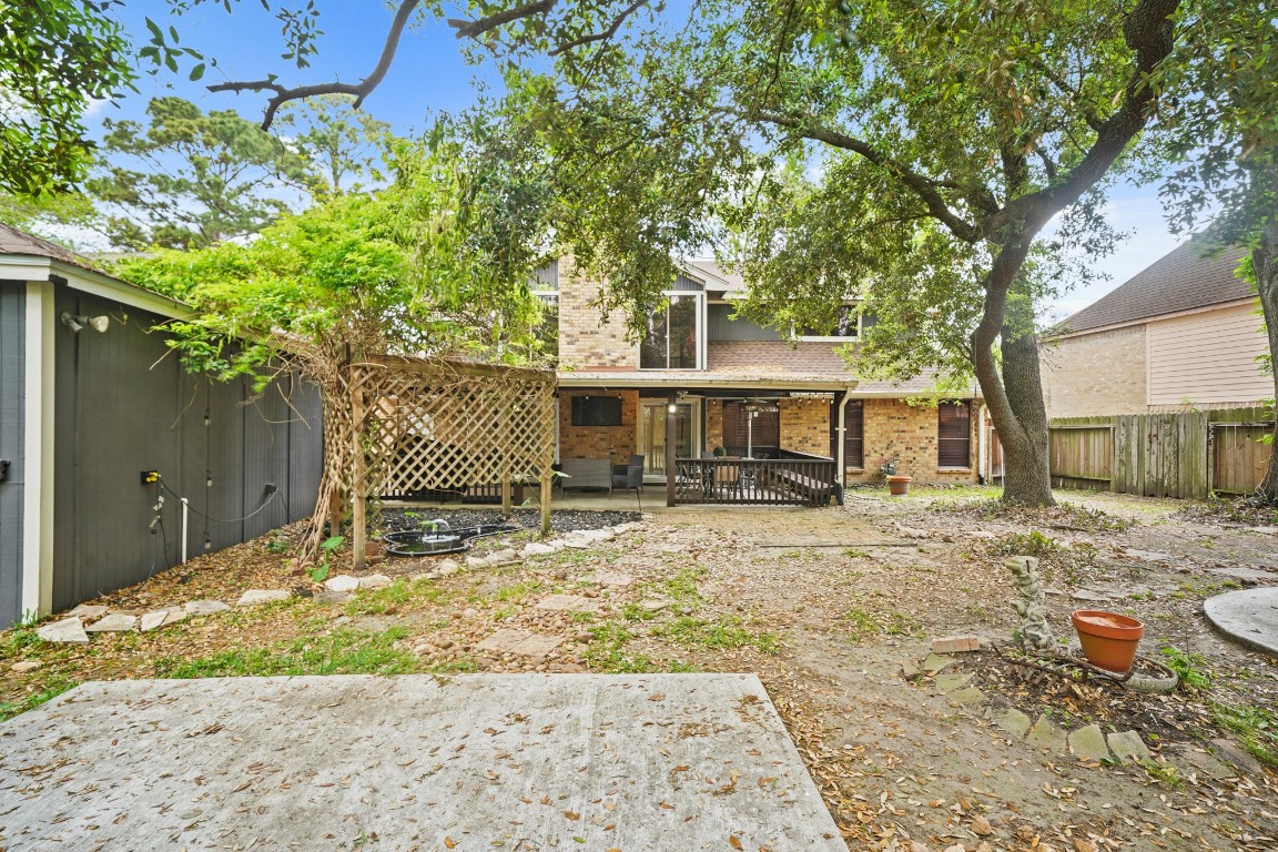 15831 Ridge Park Drive Houston, TX 77095 - Photo 19 of 26 Charming backyard with mature trees providing ample shade, a wooden deck for relaxation, and a lattice structure for potential gardening. The brick exterior of the house offers a classic look, and the fenced yard ensures privacy. Perfect for enjoying outdoor activities and entertaining.