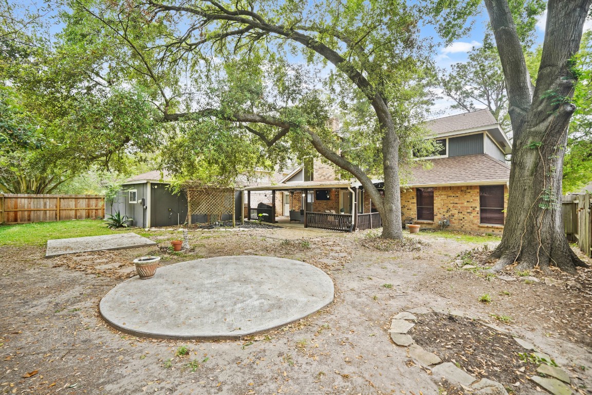 15831 Ridge Park Drive Houston, TX 77095 - Photo 20 of 26 This backyard features a spacious area with mature trees providing shade, a concrete patio, and a wooden fence for privacy. The home has a brick exterior and a covered patio area, ideal for outdoor gatherings.