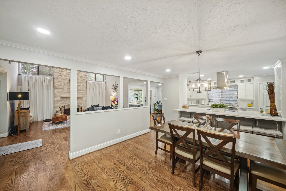 15831 Ridge Park Drive Houston, TX 77095 - Photo 8 of 26 This photo showcases an open-concept living space with hardwood floors, featuring a dining area and a modern kitchen with a large island. The living room has a cozy stone fireplace and large windows, creating a bright and inviting atmosphere.
