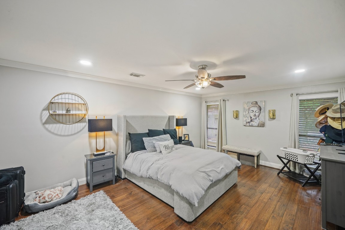 15831 Ridge Park Drive Houston, TX 77095 - Photo 9 of 26 This cozy bedroom features a spacious layout with hardwood floors, a comfortable bed, and modern ceiling fan. The room is well-lit with recessed lighting and has tasteful decor, including a wall-mounted shelf and artwork. Natural light filters through two windows dressed with curtains, creating a warm and inviting atmosphere.