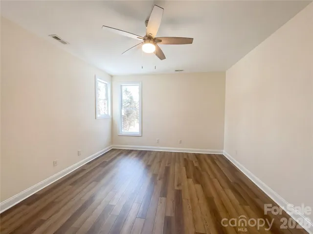 an empty room with wooden floor fan and windows