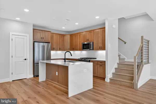 a kitchen with stainless steel appliances granite countertop a refrigerator a sink dishwasher a stove and white countertops with wooden floor