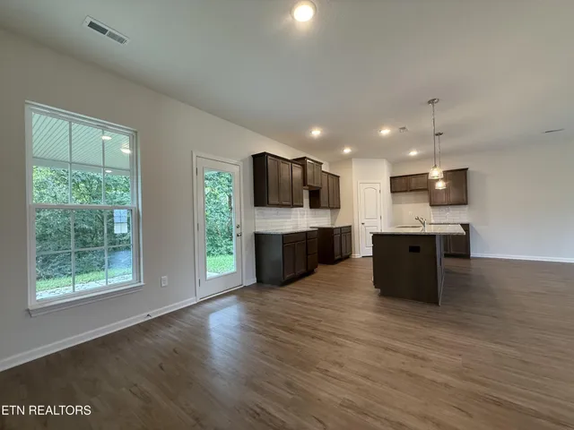 a large kitchen with stainless steel appliances granite countertop a large counter top a wooden floors and a large window