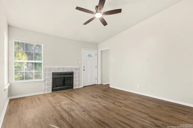 an empty room with windows fireplace and a ceiling fan