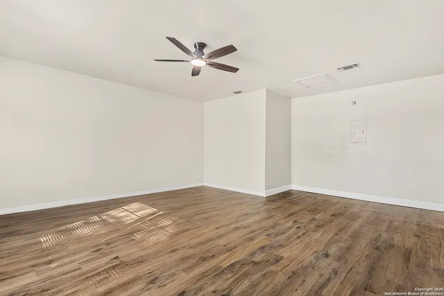 a view of an empty room with wooden floor and a ceiling fan