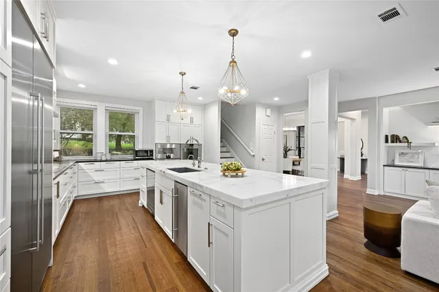 a large white kitchen with a lot of counter space a sink and stainless steel appliances