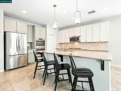 a kitchen with stainless steel appliances granite countertop a dining table chairs refrigerator and microwave