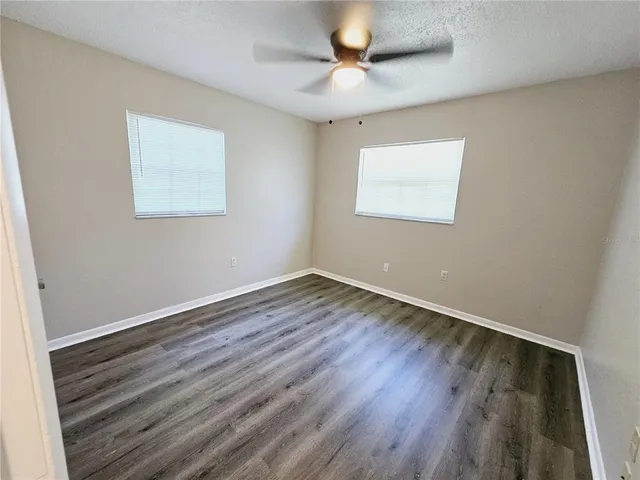 a view of an empty room with wooden floor and a ceiling fan