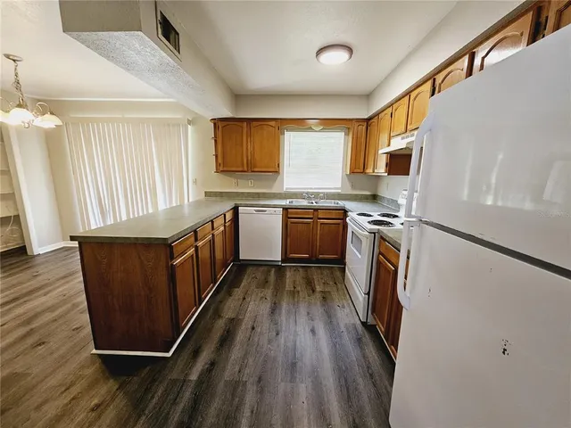 a kitchen with stainless steel appliances granite countertop a refrigerator a stove a sink dishwasher and wooden cabinets with wooden floor