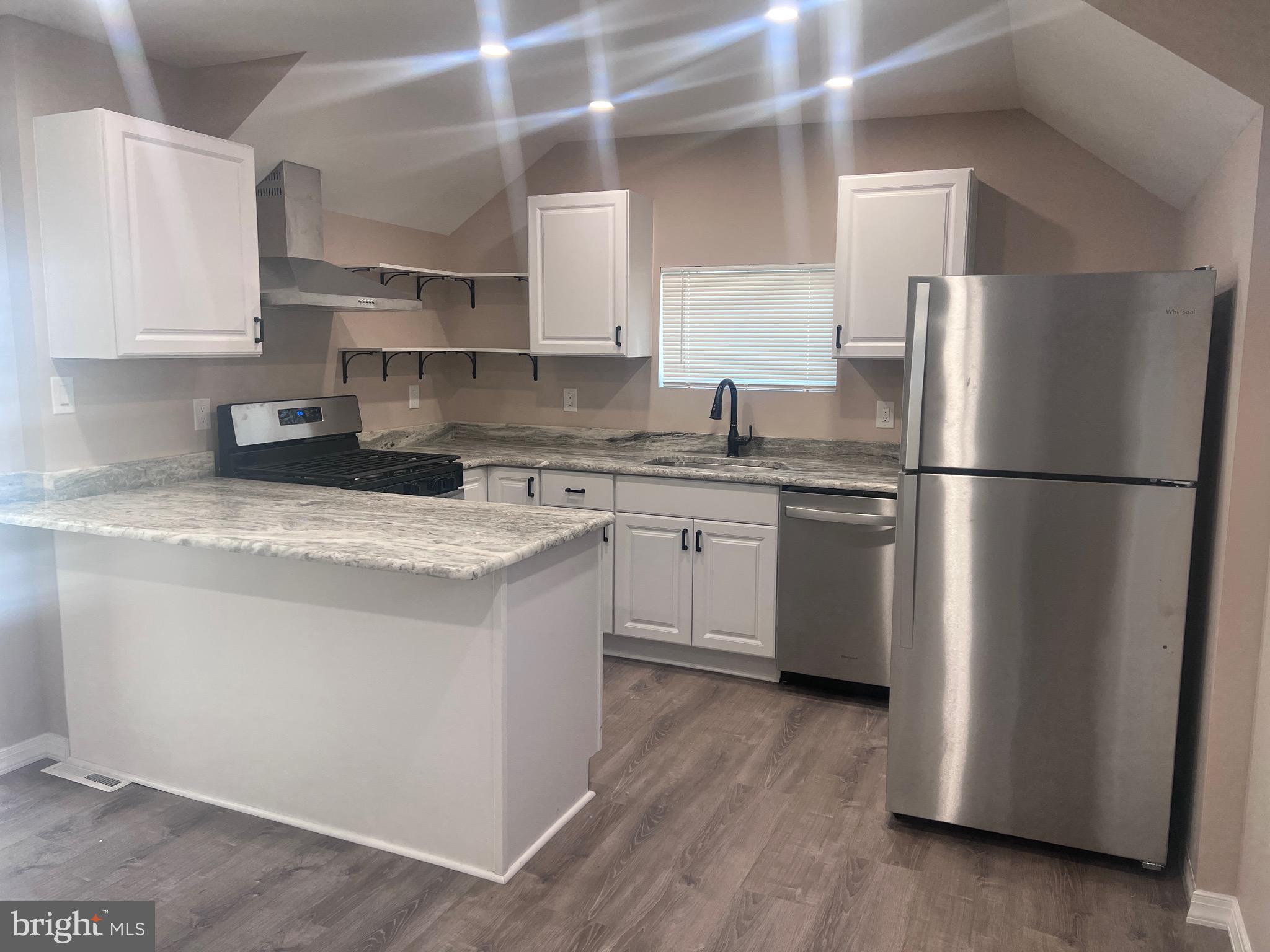 a kitchen with stainless steel appliances granite countertop a refrigerator a sink dishwasher a stove top oven a refrigerator with white cabinets and wooden floor
