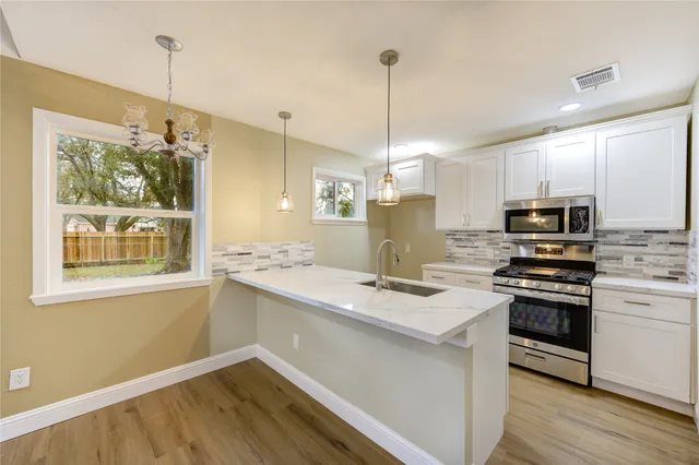 a kitchen with stainless steel appliances granite countertop a sink a stove a refrigerator and island with wooden floor