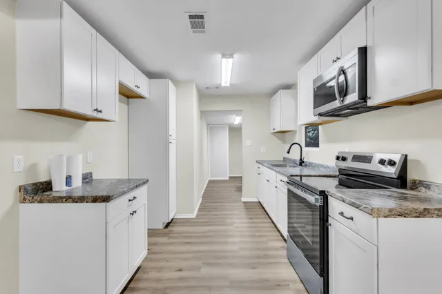 a kitchen with stainless steel appliances granite countertop a stove top oven a sink dishwasher and a microwave oven with white cabinets