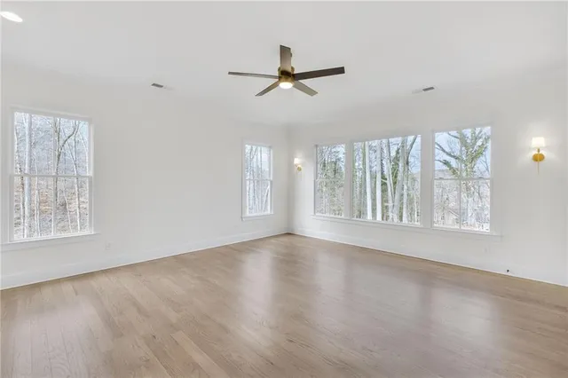 an empty room with wooden floor fan and windows