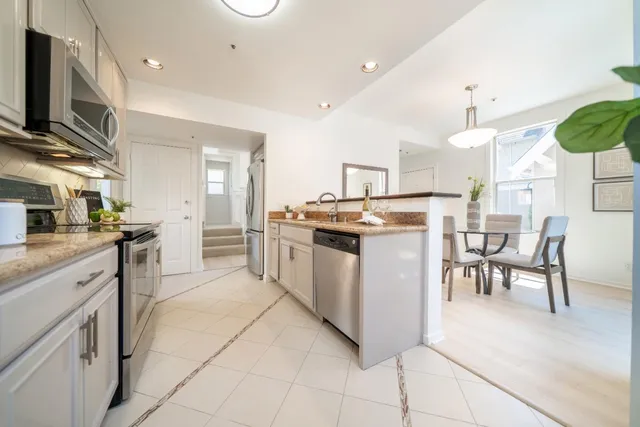 a kitchen with stainless steel appliances granite countertop a stove top oven a sink dishwasher a dining table and chairs with wooden floor