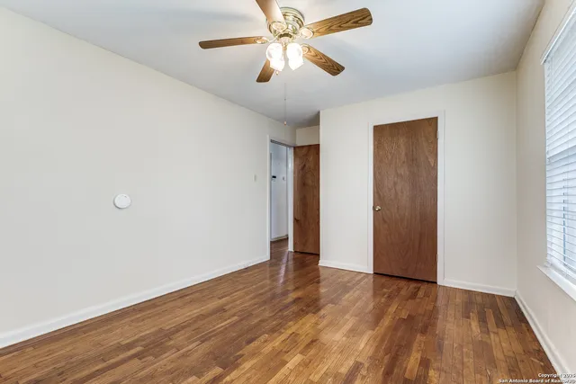 an empty room with wooden floor closet and windows