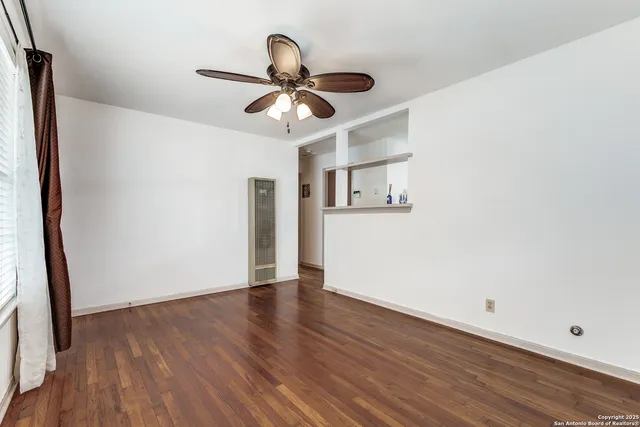 a view of an empty room with wooden floor and a ceiling fan