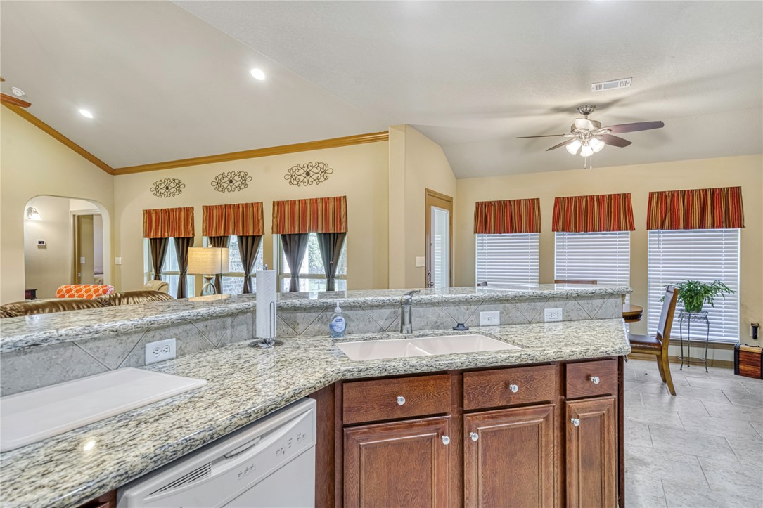 9945 Oxford Cemetery Road Madisonville, TX 77864 - Photo 15 of 42 Kitchen with lofted ceiling, dishwasher, light stone counters, brown cabinets, and arched walkways