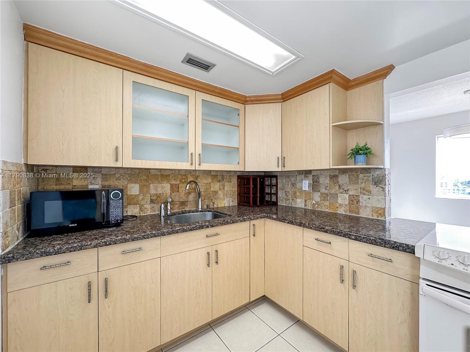 8001 Crespi Boulevard, Unit 7A Miami Beach, FL 33141 - Photo 6 of 25 a kitchen with granite countertop white cabinets and white appliances