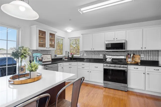 a kitchen with stainless steel appliances kitchen island granite countertop a sink dishwasher stove and white cabinets with wooden floor
