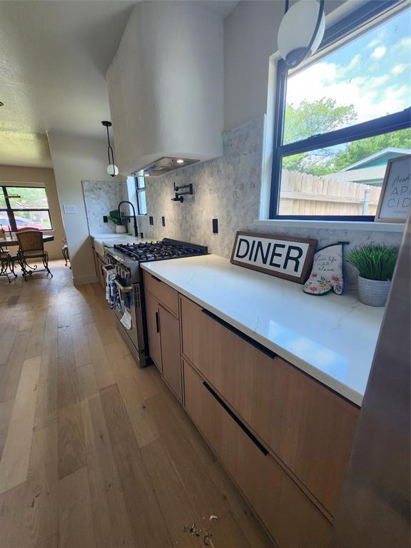 2908 Washington Street Commerce, TX 75428 - Photo 9 of 29 Modern kitchen featuring light wood-finish cabinetry with linear hardware, a built-in stainless steel range, and a custom-designed range hood