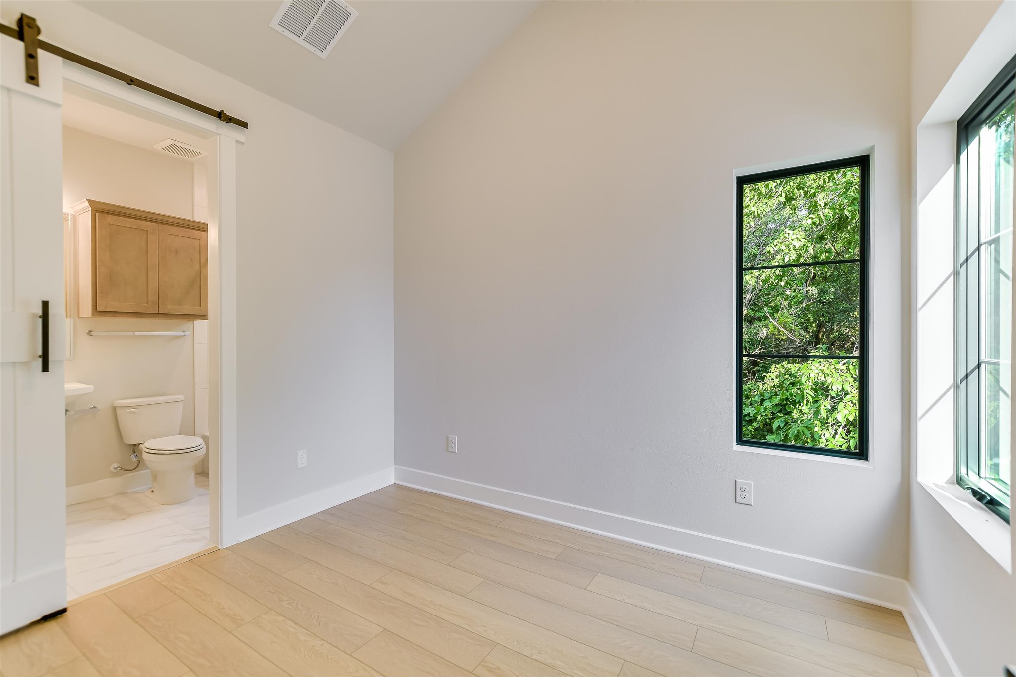 114 Lightsey Road, Unit 2 Austin, TX 78704 - Photo 13 of 14 Unfurnished bedroom featuring ensuite bath, lofted ceiling, a barn door, and light wood-type flooring