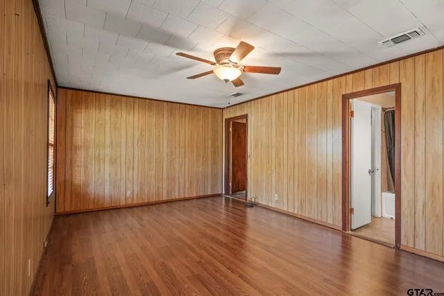an empty room with wooden floor chandelier fan and windows