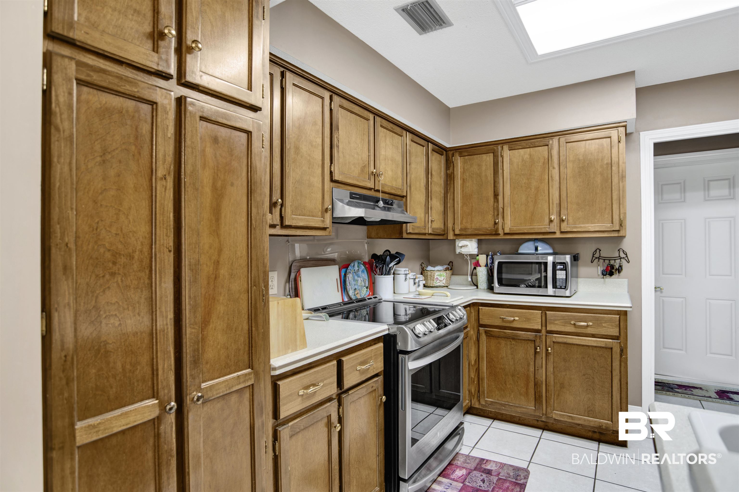 107 Virginia Circle Daphne, AL 36526 - Photo 15 of 47 Kitchen featuring wood cabinetry, white countertops, stainless steel range with overhead microwave, and white tile flooring