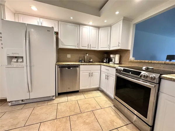 a white kitchen with granite countertop a stove top oven a sink and cabinets