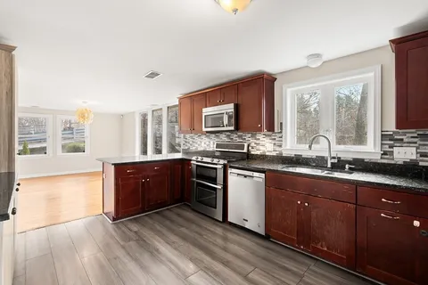 a large kitchen with stainless steel appliances granite countertop a sink stove and wooden cabinets