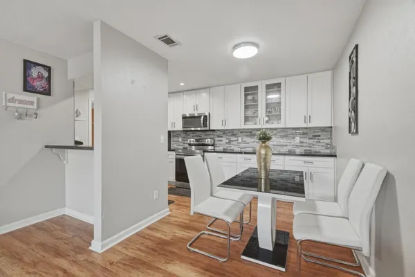 a kitchen with stainless steel appliances granite countertop a stove a refrigerator and white cabinets with wooden floor