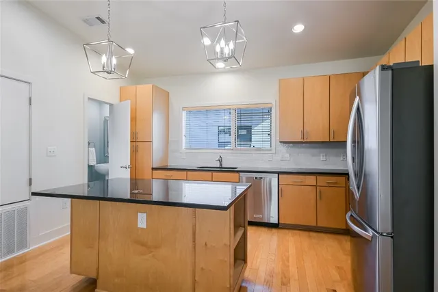 a kitchen with stainless steel appliances granite countertop a refrigerator a sink dishwasher a stove and a dining table with wooden floor