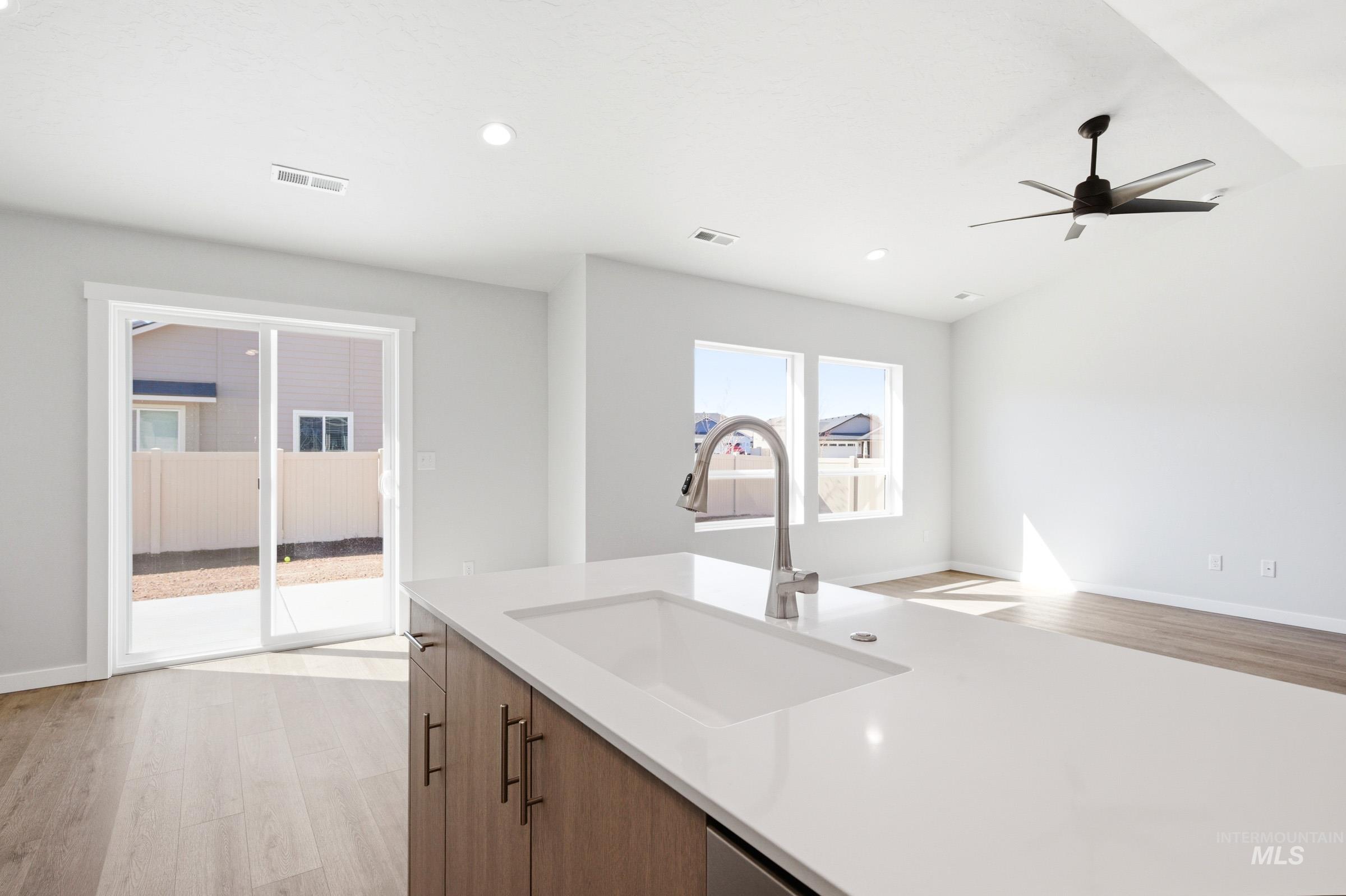 12877 Decatur Street Nampa, ID 83651 - Photo 6 of 22 Kitchen island featuring an integrated sink with a gooseneck faucet, light-toned countertop, and wood-finish cabinetry with brass hardware
