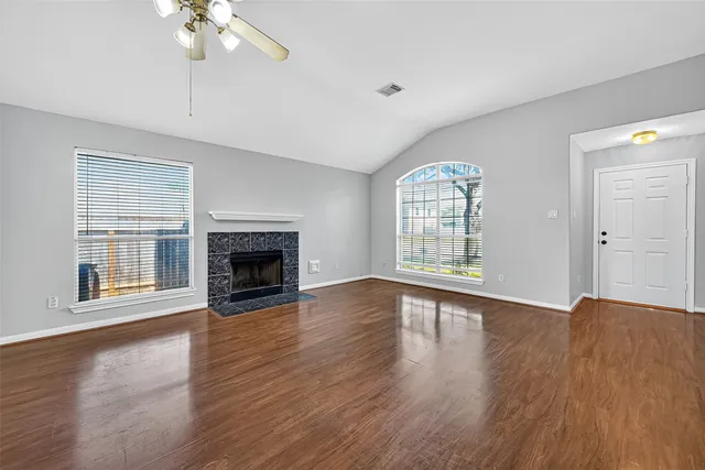 an empty room with wooden floor chandelier fan and windows