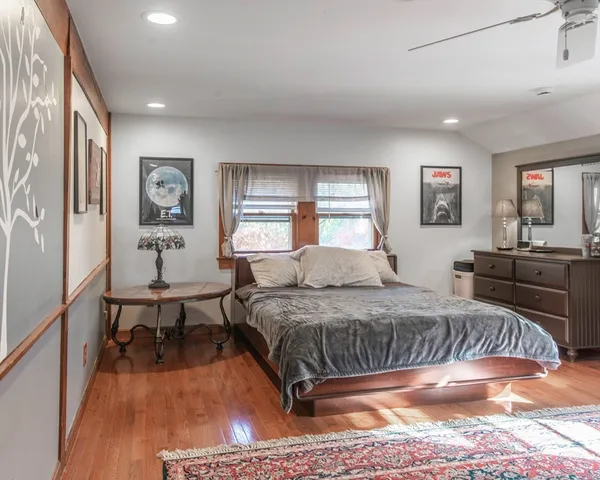a bedroom with a bed a table and dresser with wooden floor