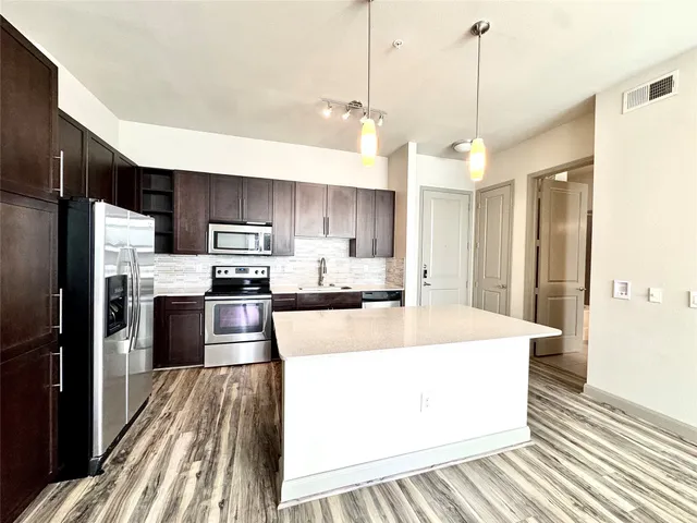 a large kitchen with stainless steel appliances kitchen island granite countertop a refrigerator a oven a sink with a countertop and chairs