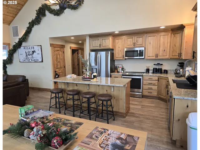 a kitchen with stainless steel appliances kitchen island granite countertop a sink dishwasher a microwave oven and a dining table with wooden floor