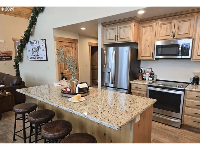 a kitchen with stainless steel appliances granite countertop a stove a refrigerator a sink a dining table and chairs with wooden floor