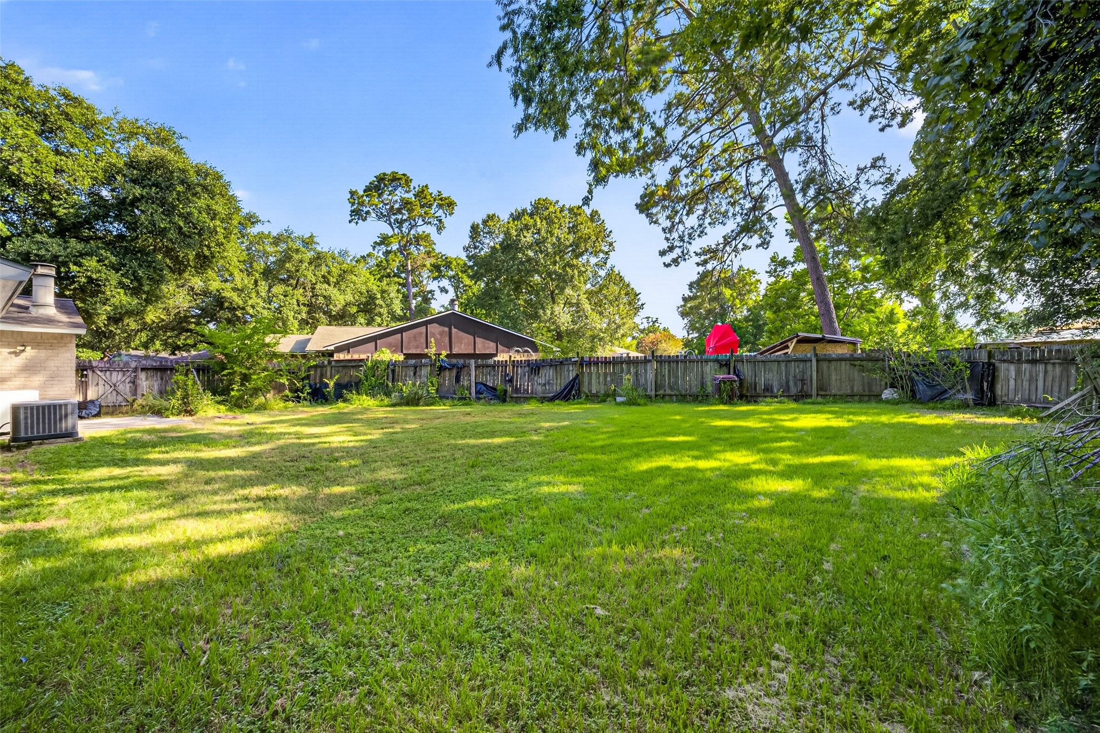 22926 Millgate Drive Spring, TX 77373 - Photo 32 of 34 Spacious backyard with lush grass, bordered by a wooden fence and surrounded by mature trees, offering privacy and ample space for outdoor activities.